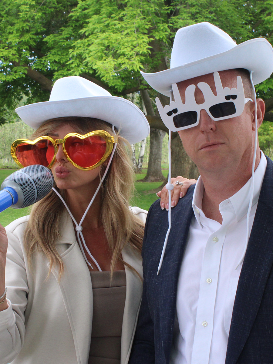 A classy couple in their 40s wearing stylish props like funny glasses and hats at a Kelowna photo booth.