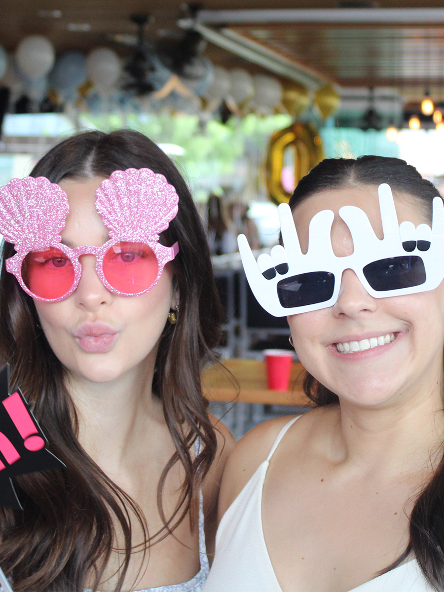 Two girls posing with fun props inside a professional Kelowna photo booth.