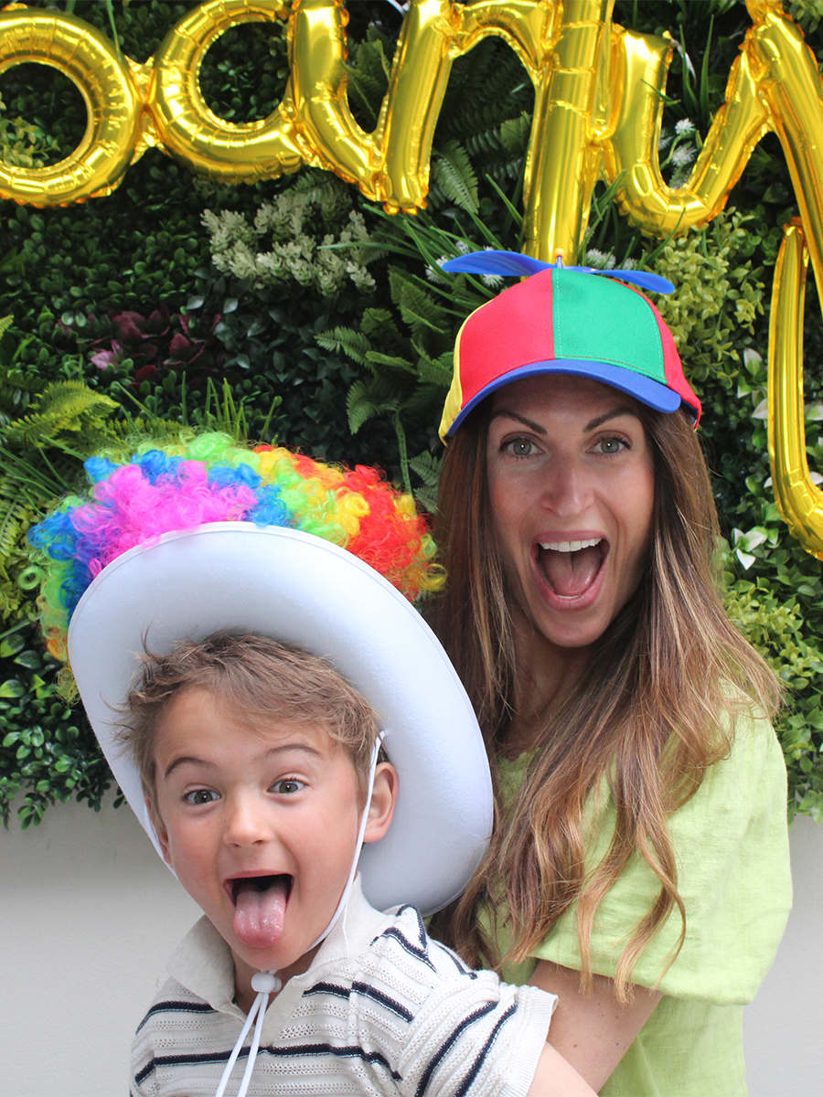 A mom and son making silly faces and playing with a funny hat at a photo booth.