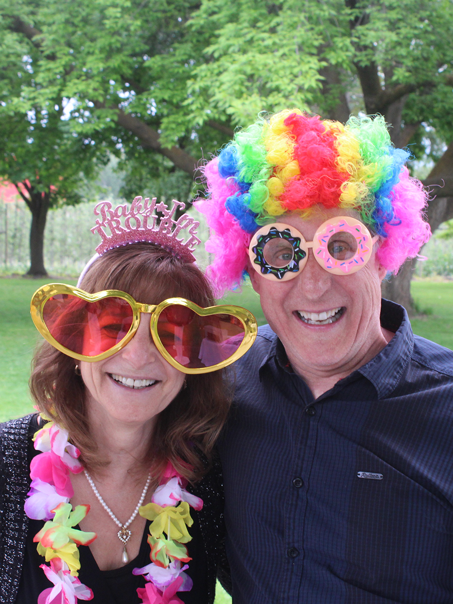 A married couple in their 60s having fun in a Kelowna photo booth, wearing silly wigs and glasses.